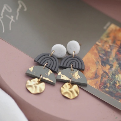 Brincos em cores cinza e branco com detalhes dourados sobre fundo rosa e papel