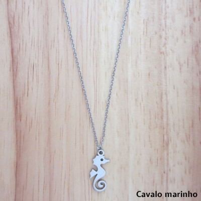 Colar com pendente em forma de cavalo marinho prateado sobre madeira clara