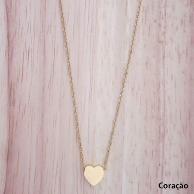 Colar dourado com pendente em forma de coração sobre madeira clara