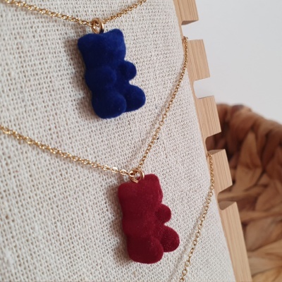 Colares com pendentes em forma de ursinho azul e vermelho, texturizados, em expositor de tecido bege