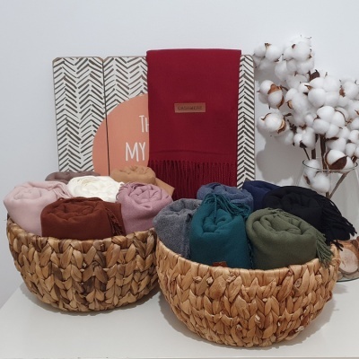 Dois cestos de vime com mantas coloridas enroladas numa superfície branca, com decorações e placas ao fundo