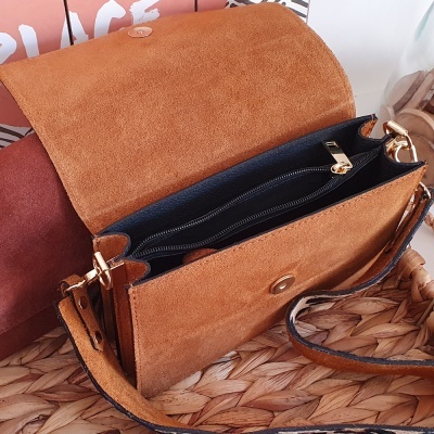 Mala castanha em camurça com interior preto e fecho dourado aberta sobre tecido de ráfia