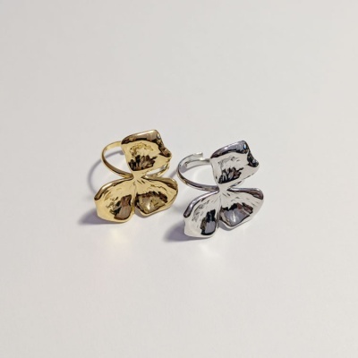Dois anéis em metal dourado e prateado com design de quatro pétalas grandes sobre superfície branca