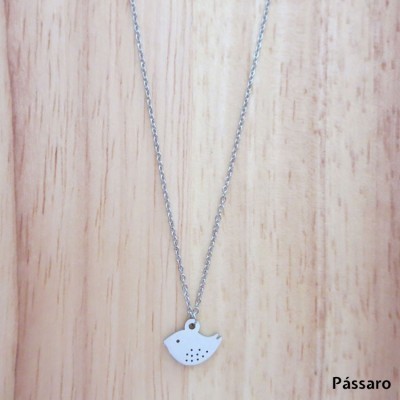 Colar com pendente de pássaro branco sobre madeira clara.