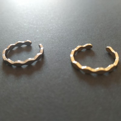 Dois anéis metálicos ondulados, um prateado e outro dourado, sobre fundo preto