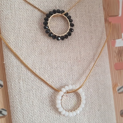 Dois colares com pendentes circulares e pedras pretas e brancas em fundo de tecido bege