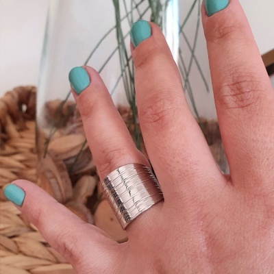 Anel prateado largo com linhas horizontais numa mão com unhas azuis