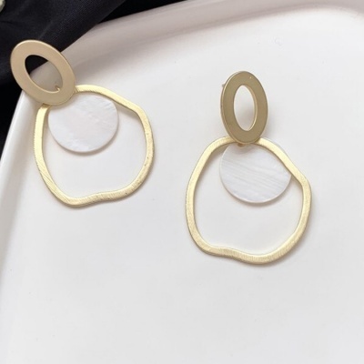 Brincos geométricos dourados com formas oval e círculo sobre prato branco