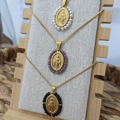 Três colares dourados com medalhões e diferentes contas expostos em suporte de madeira