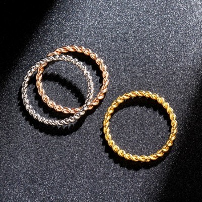 Três anéis de metal torcido em prata, dourado e cobre sobre fundo preto texturizado