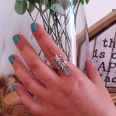 Anel prateado em forma de folha em mão feminina com unhas verdes-azuladas e objeto decorativo em madeira