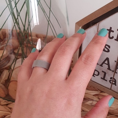 Anel prateado em mão com unhas verdes e fundo decorativo