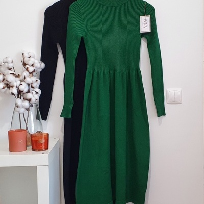 Dois vestidos de malha, um verde e um preto, pendurados numa parede ao lado de um vaso com algodão e velas.