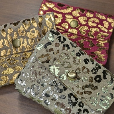 Três carteiras pequenas de padrão animal print brilhante com botões metálicos sobre mesa de madeira