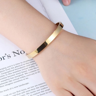 Pulseira fina de metal dourado num braço sobre papel branco