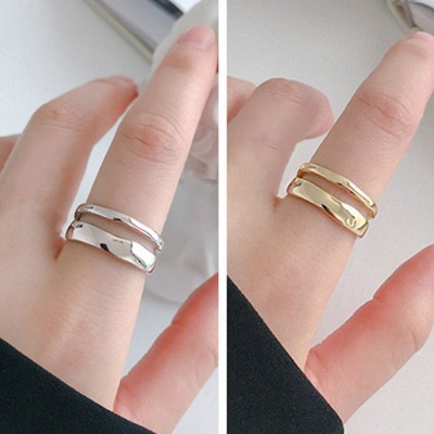 Dois anéis ondulados, um prateado e um dourado, usados em dedos