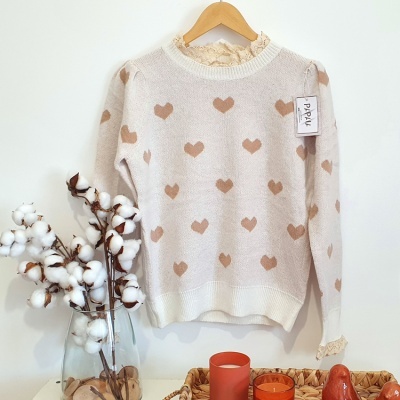 Camisa de malha creme com corações castanhos pendurada e vaso com algodão ao lado