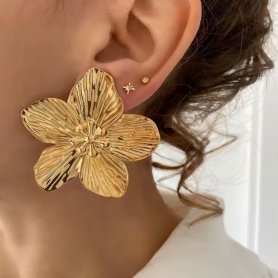 Brinco flor dourado grande com textura e dois brincos pequenos dourados na orelha