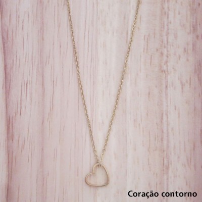 Colar dourado com pendente coração contorno sobre fundo de madeira clara