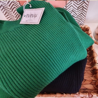 Suéteres verde e preto em cesta de vime com etiqueta PAPIA
