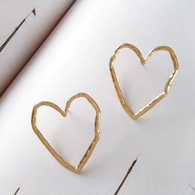 Par de brincos dourados em forma de coração sobre uma página branca