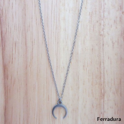 Colar prateado com pendente de ferradura sobre madeira clara