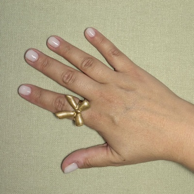 Anel dourado com design tubular usado no dedo médio de mão com unhas nude sobre fundo bege