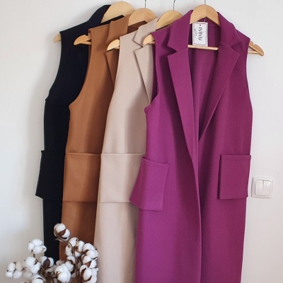 Casacos sem mangas em várias cores pendurados em cabides junto a um ramo de algodão