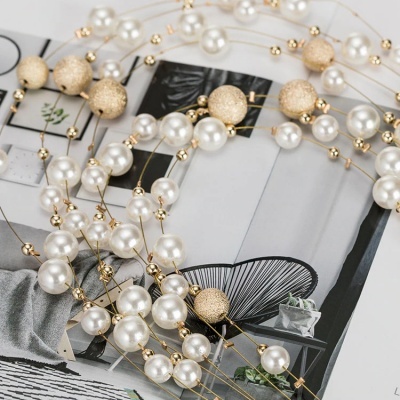 Colar decorativo com pérolas brancas e esferas douradas sobre revista aberta