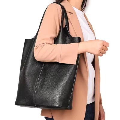 Bolsa tote preta de pele com textura granulada transportada por mulher de blazer bege