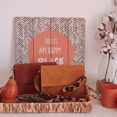 Display decorativo com texto, duas bolsas castanhas, castiçal de pêra, vaso com algodão e vela coral sobre uma mesa.