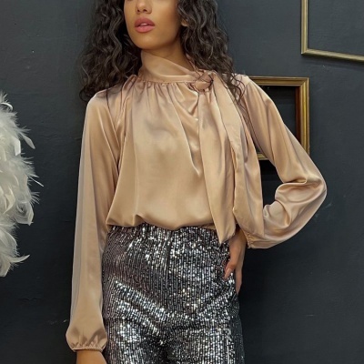 Blusa acetinada bege com mangas longas e laço, calças prateadas brilhantes com lantejoulas