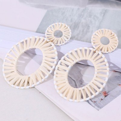 Brincos circulares trançados em tons creme e branco sobre livro e superfície branca