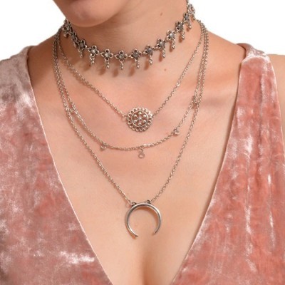 Colares prateados em camadas com diversos pendentes usados sobre vestido de veludo rosa claro