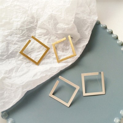 Dois pares de brincos quadrados angulares em metal dourado e prateado sobre papel branco amassado e prato azul.