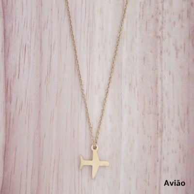 Colar com pendente em forma de avião dourado sobre fundo de madeira clara