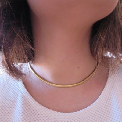 Colar dourado rígido no pescoço de pessoa com camisola branca