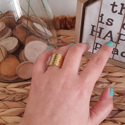 Mão com anel dourado largo e unhas azuis sobre mesa decorativa