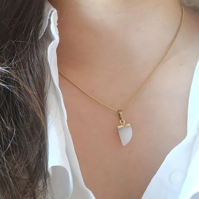 Colar dourado com pendente branco em formato de dente, usado por pessoa com camisa branca.