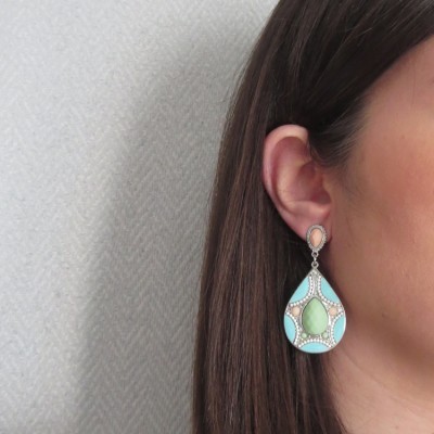 Brinco pendente azul e verde com detalhes brilhantes, usado na orelha esquerda