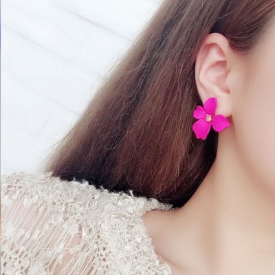 Brinco flor rosa com centro amarelo na orelha direita de mulher com cabelo castanho e roupa bege texturada