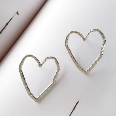 Brincos em forma de coração prateados com acabamento martelado sobre fundo branco