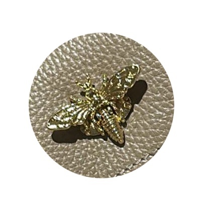 Broche dourado em forma de abelha sobre superfície de couro bege