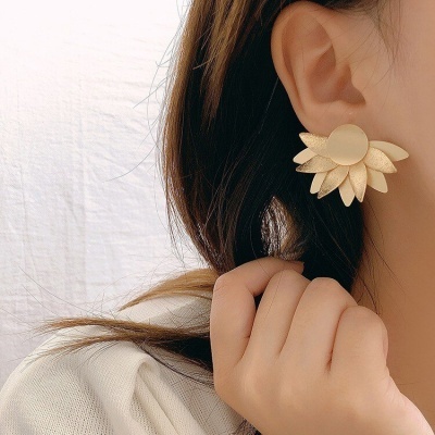 Brincos dourados em forma de flor com pétalas texturizadas na orelha
