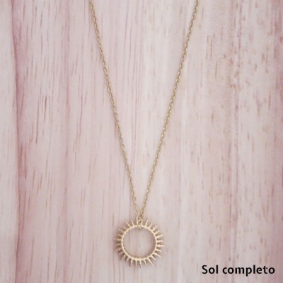 Colar dourado com pendente circular em forma de sol sobre fundo de madeira clara