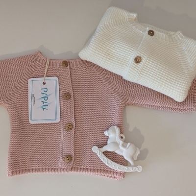 Dois casacos de malha para bebé rosa e branco com botões, etiqueta PAPPYL e cavalo de baloiço branco