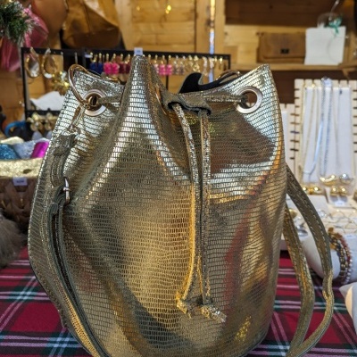 Mala tipo saco dourada com textura reptiliana exposta em loja