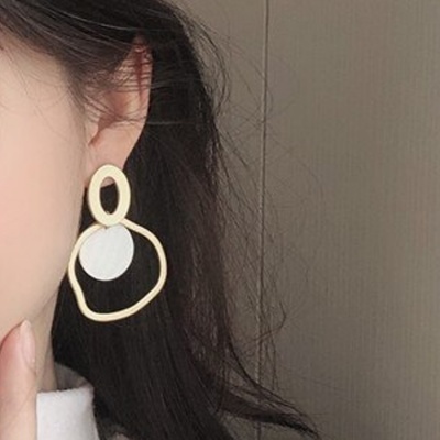 Brinco dourado com formas geométricas e círculo branco pendurado na orelha de mulher