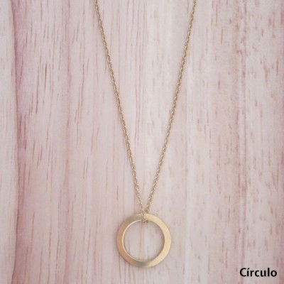 Colar dourado com pendente redondo circular sobre fundo de madeira clara.