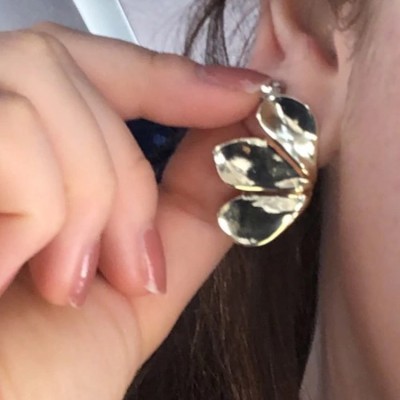 Brinco metálico em forma de borboleta prateada na orelha de uma mulher.